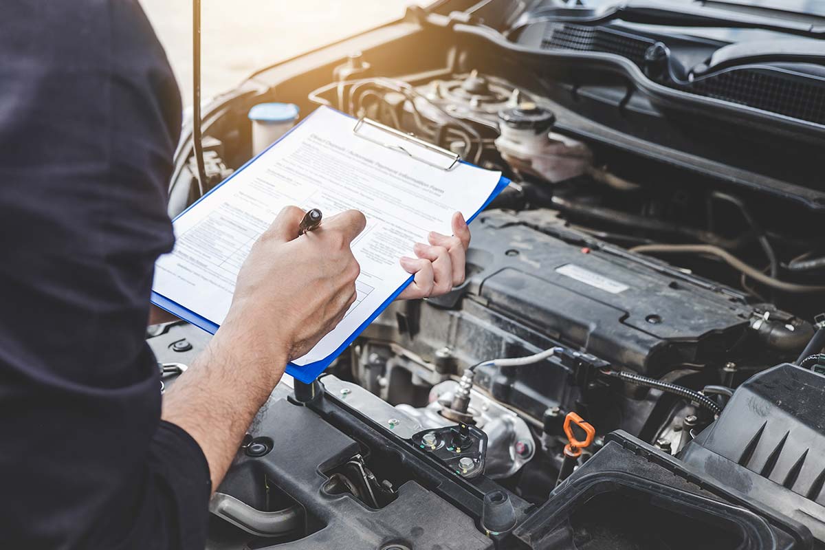 Person holding a clipboard and writing notes while inspecting a car engine.